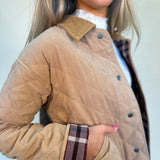 close-up detail shot of quilted barn jacket showing plaid detail on rolled up sleeve and corduroy collar and button details. shear boutique