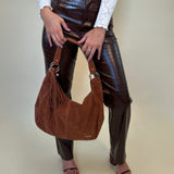 Person holding a brown leather handbag wearing cassie brown pants against a plain background