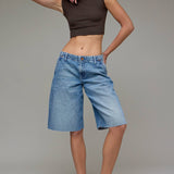 Woman wearing a brown sleeveless top and blue denim shorts against a plain background