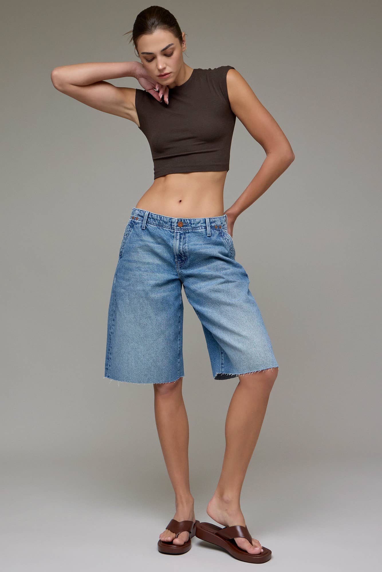 Woman wearing a brown sleeveless top and blue denim shorts against a plain background