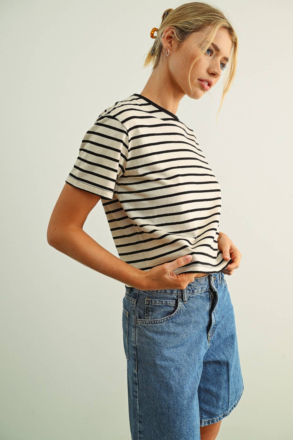 Woman wearing a striped shirt and denim shorts against a plain background