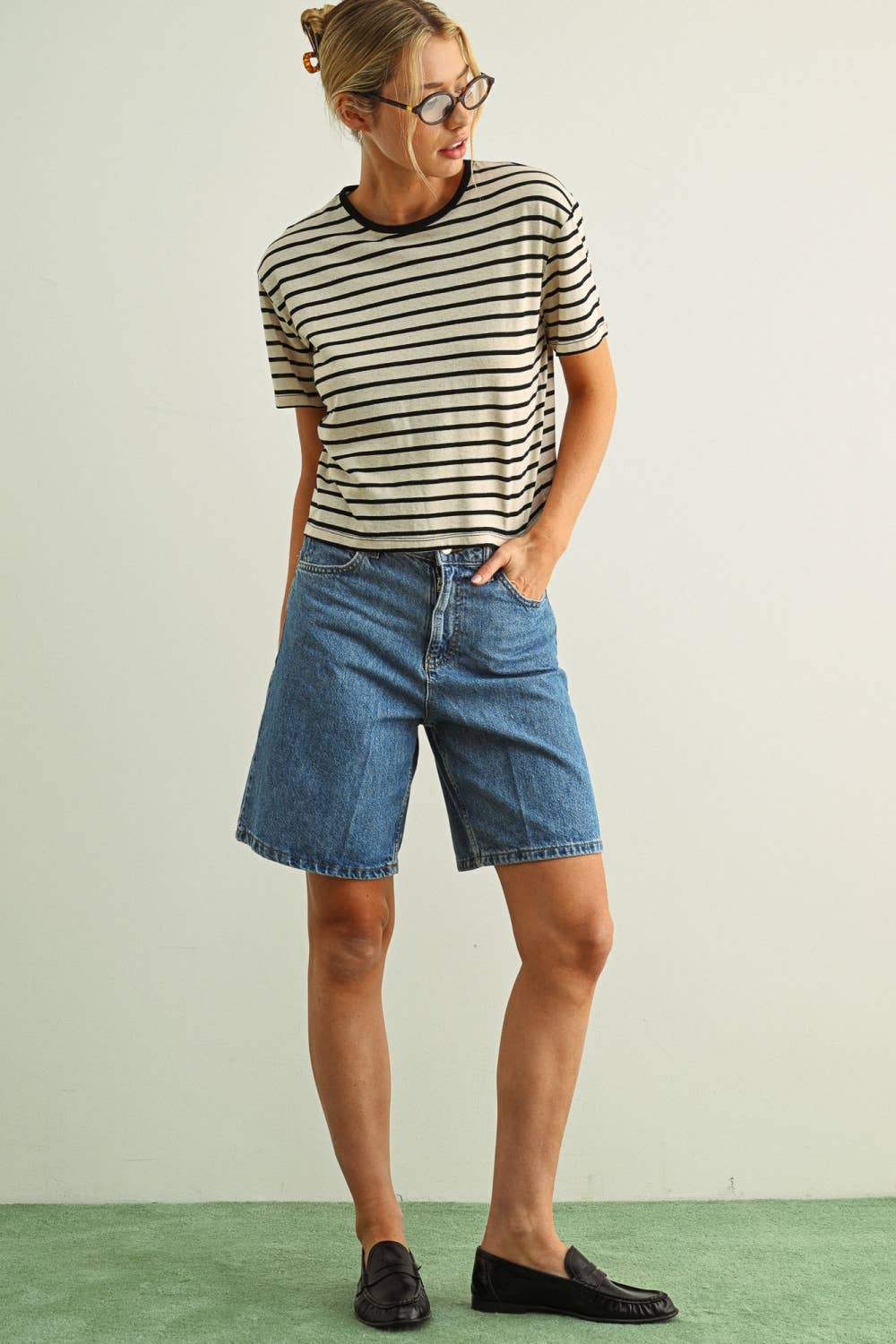 Person wearing a striped shirt and denim shorts on a plain background
