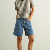 Person wearing a striped shirt and denim shorts on a plain background