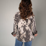 A woman viewed from behind wearing a long-sleeve button-up shirt with a black and white cow-print pattern, paired with blue jeans, against a plain light gray studio background.