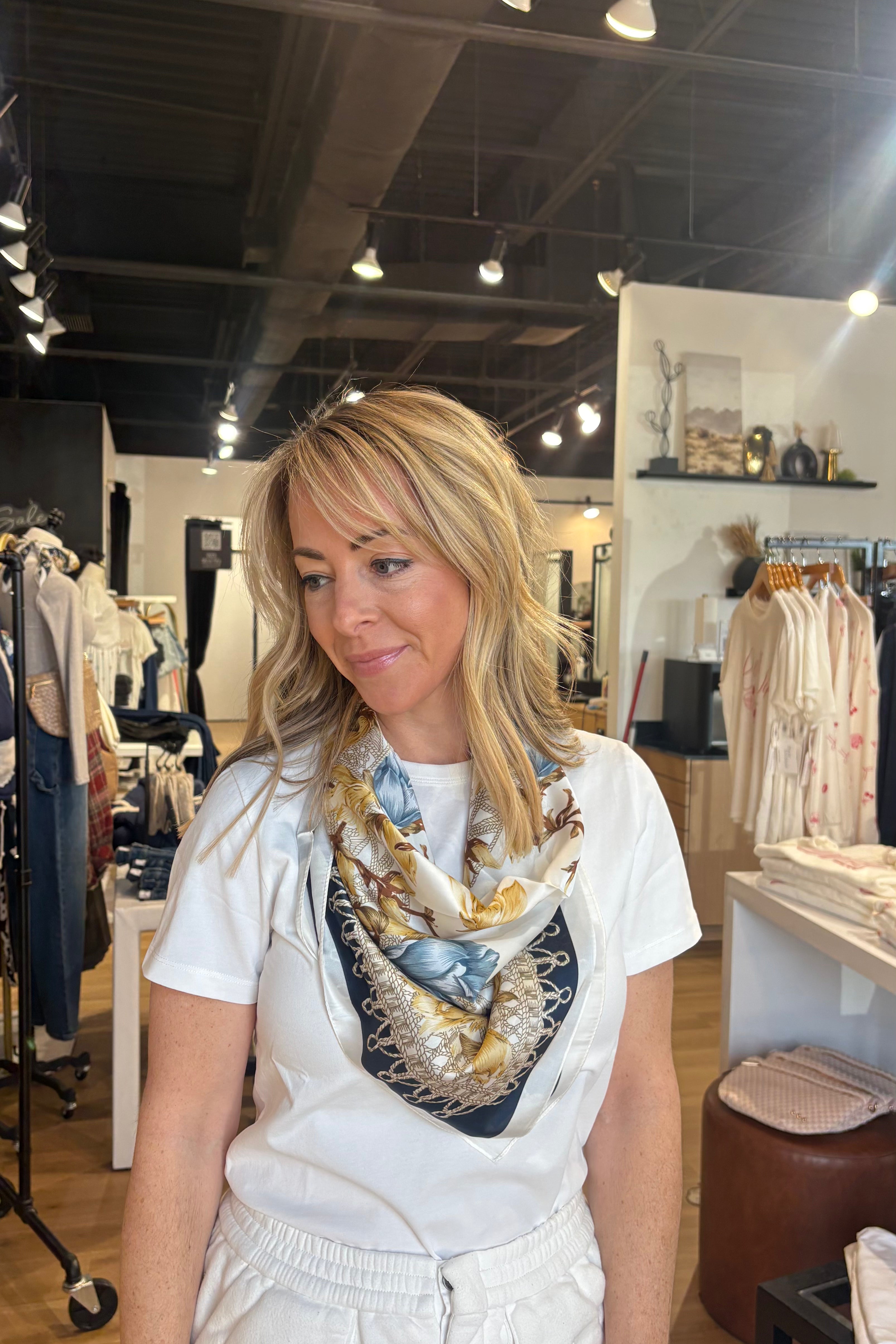 Woman wearing a white shirt and patterned scarf in a clothing store.