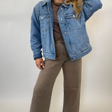 Woman wearing a denim jacket, brown top, and pants on a plain background