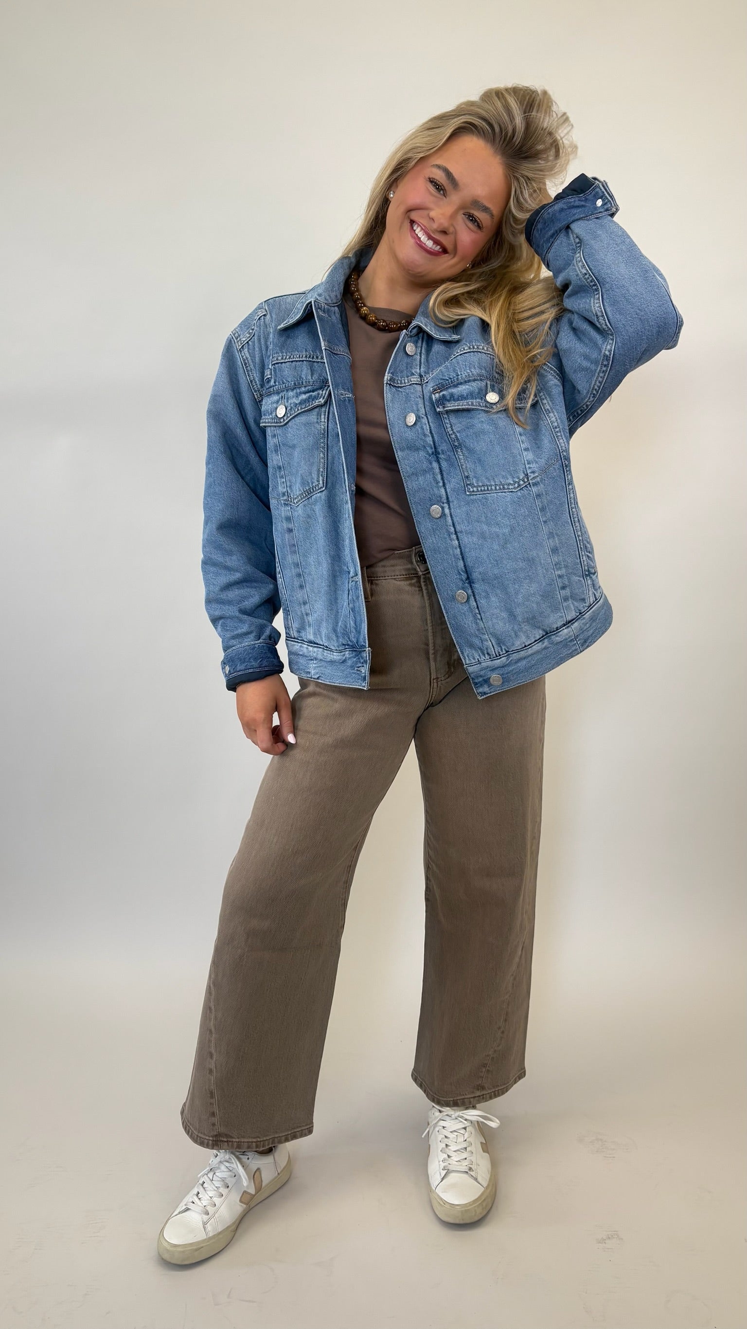 Woman wearing a denim jacket, brown top, and pants on a plain background