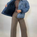 Person wearing a blue denim jacket, brown top, and wide-leg jeans on a plain background