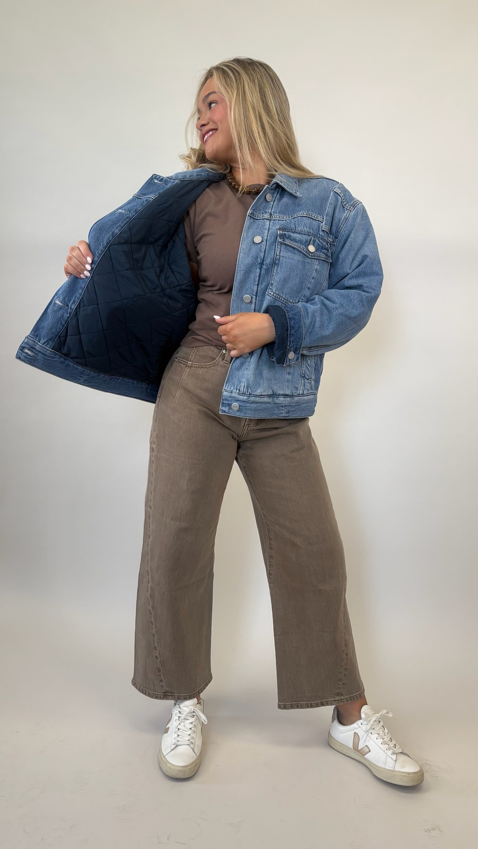 Person wearing a blue denim jacket, brown top, and wide-leg jeans on a plain background