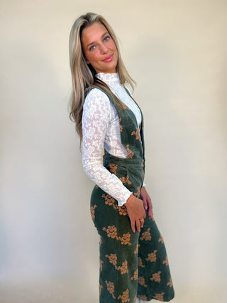 side view of green corduroy jumpsuit. low side cut, deep plunging neckline. Worn with white long sleeve knit textured top. Shear Boutique fall 
