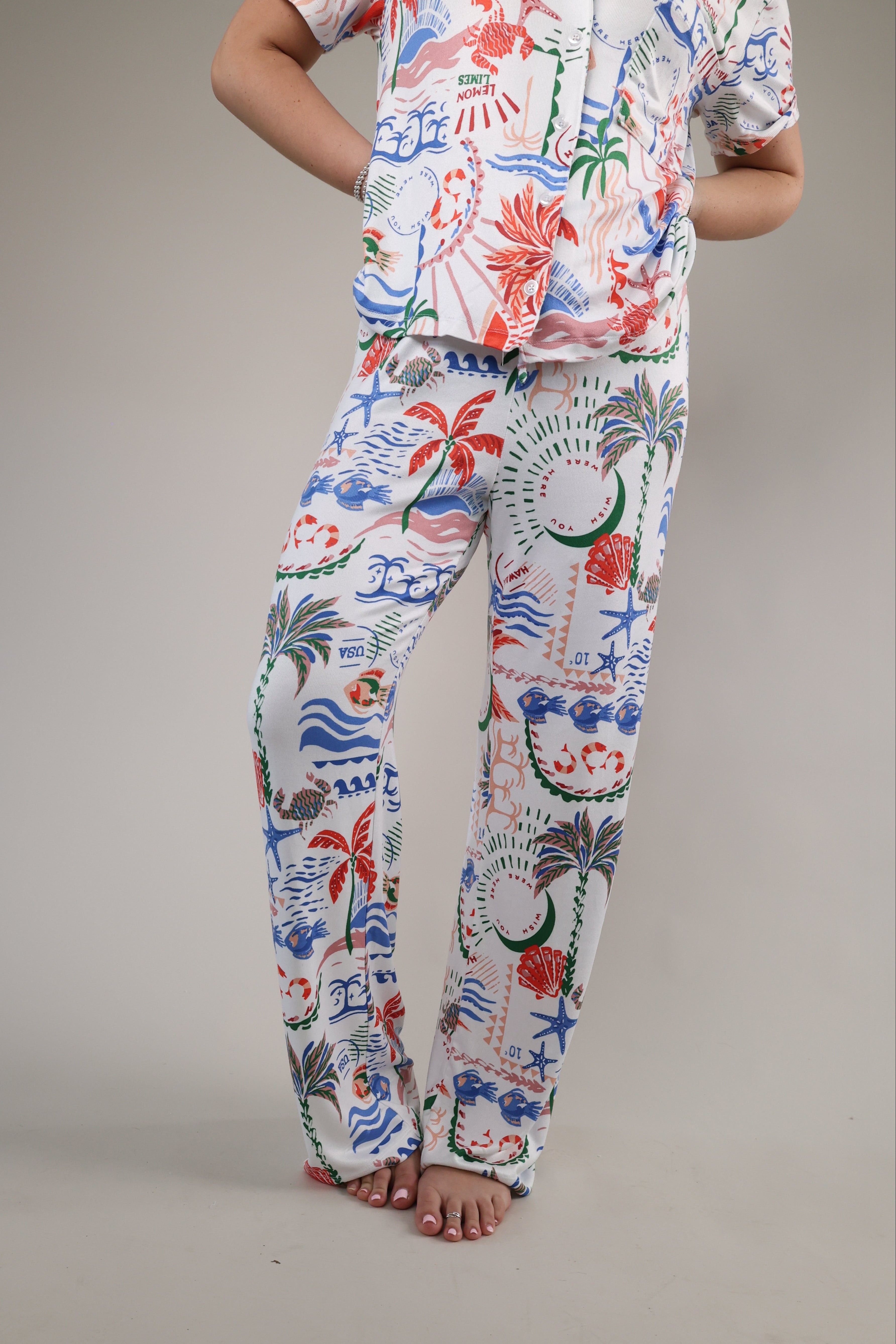 Relaxed fit pajama pants featuring tropical artwork with coral, palm trees, and ocean-inspired accents on a soft white background.