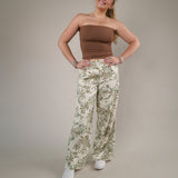 Wide-leg tropical print linen pants featuring a soft neutral background with green palm-inspired detailing and an airy relaxed fit.